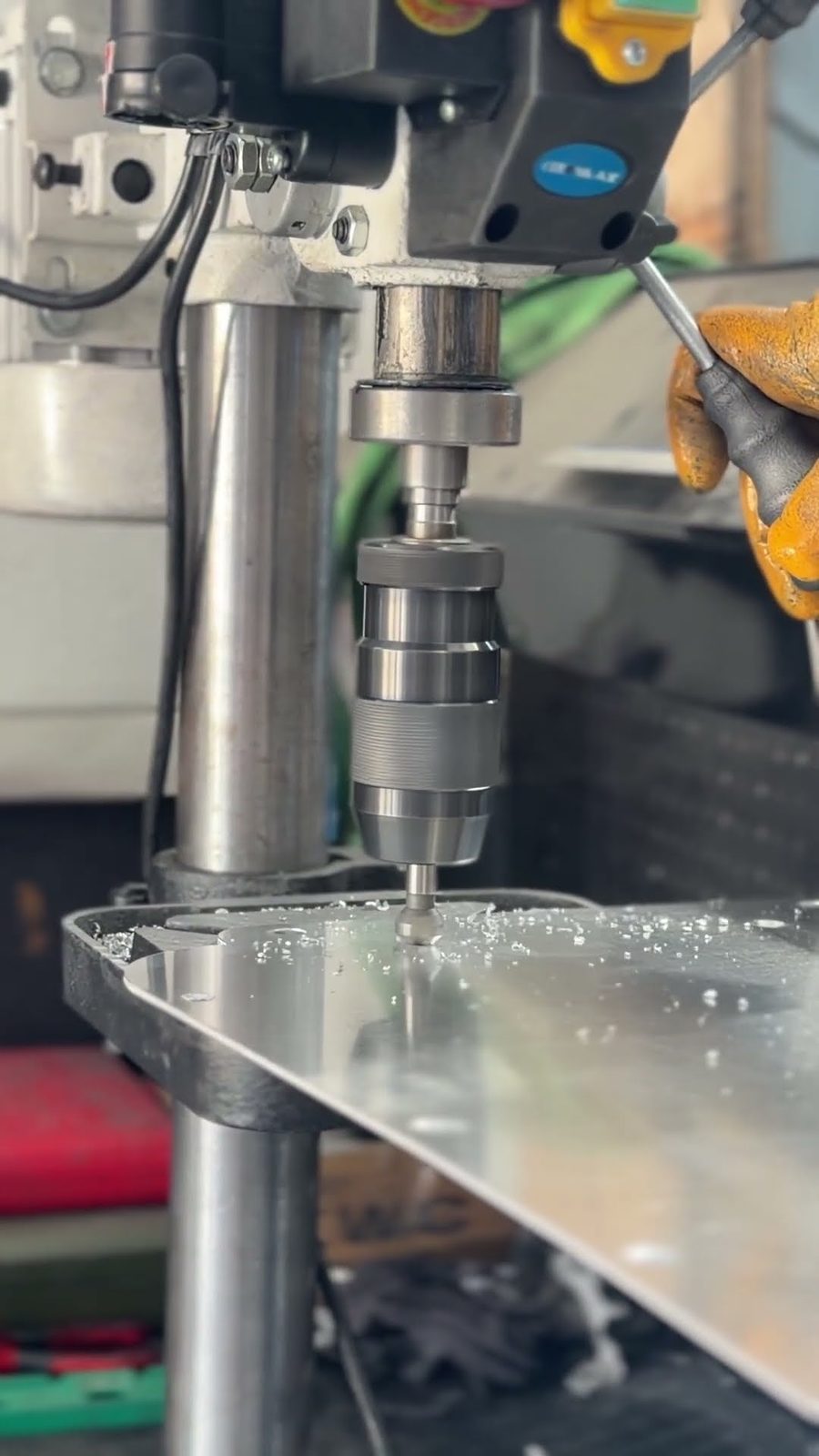 Mounting holes being drilled into an aluminium body panel on a bench drill, swarf curls scattered across the surface