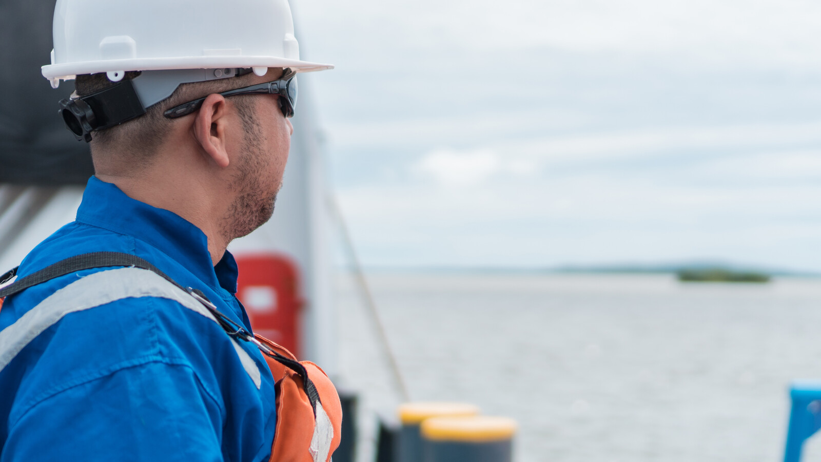 Een dekofficier met witte helm en blauwe overall die vanaf de reling van een schip uitkijkt over zee